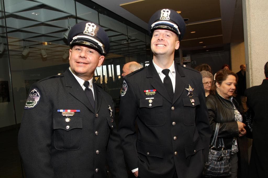 Zwei lachende Beamte im Vordergrund, mit Menschen in der Mitte, Glasfenster links, Lampen und Decke oben und Säulen und Menschen rechts.