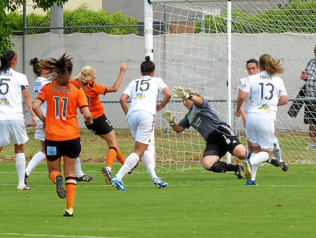 Eine Gruppe von Frauen, die auf dem Boden ein Spiel spielen, mit einem Maschendrahtzaun und Bäumen im Hintergrund.