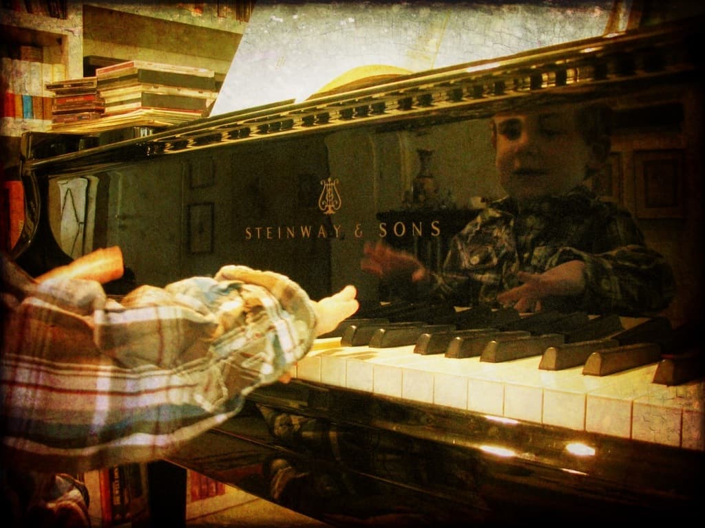 Ein Kind sitzt an einem Piano und spielt die Tasten.