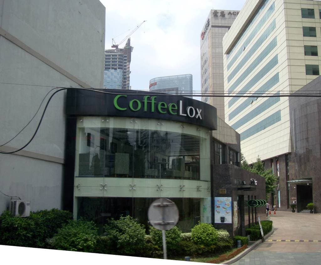 Ein Geschäftsgebäude mit ein paar Pflanzen davor, umgeben von vielen hohen Gebäuden und einigen Drähten.