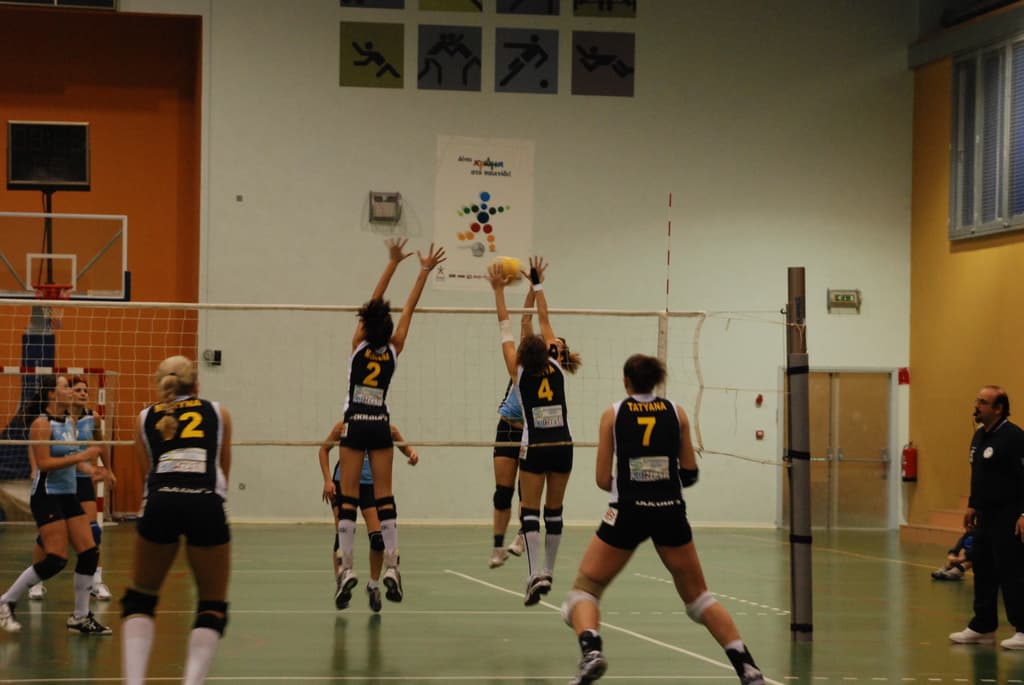 Ein Volleyballfeld mit aktiv spielenden Spielern, mit einem Basketballkorb, Fenstern und einer Tür im Hintergrund.