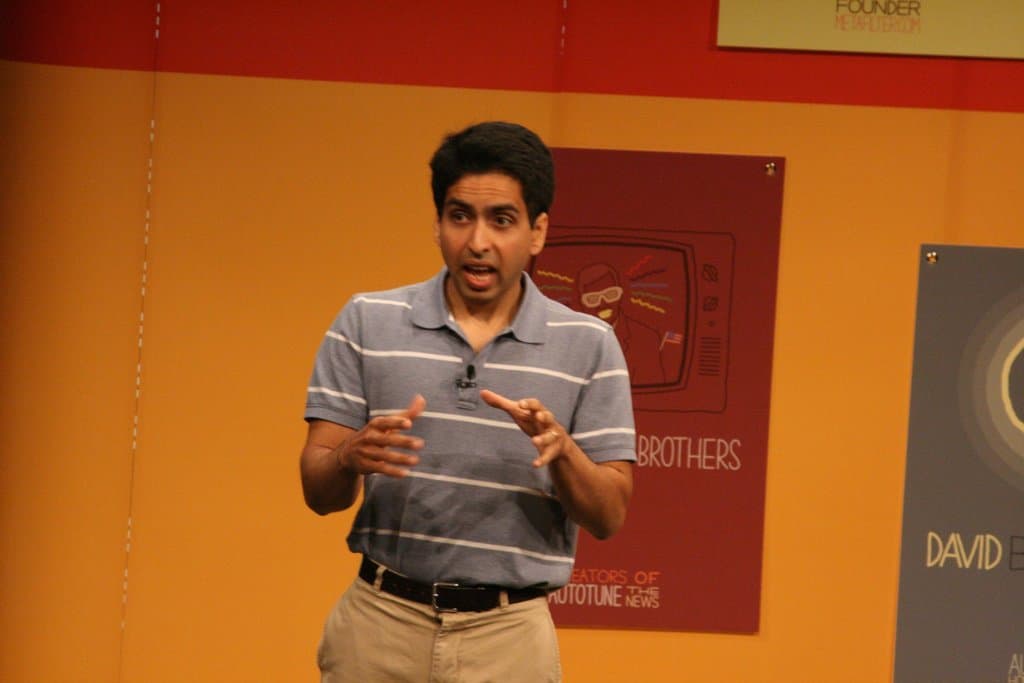 Ein Mann steht auf der Bühne und spricht vor einer Wand mit Postern.