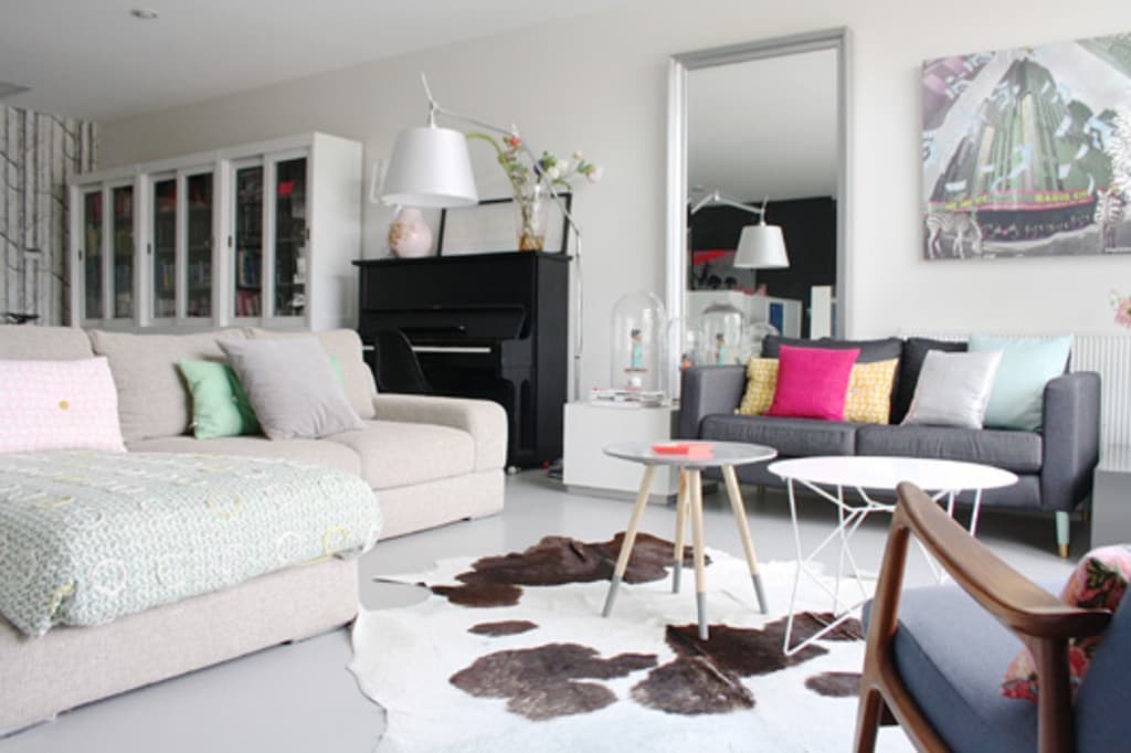 Ein Wohnzimmer mit zwei Sofas, zwei Tischen, einer Lampe, einem Kissen, einem Spiegel, einem Musikinstrument und einer Vitrine an der Wand.