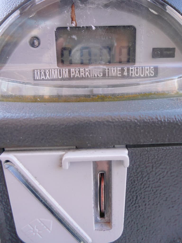 Ein Parkscheinautomat mit der Aufschrift "Maximale Parkdauer 4 Stunden" und einem Münzschlitz mit einer Münze.