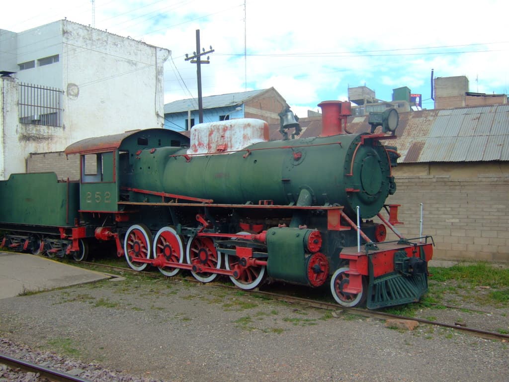 Ein Zug im Vordergrund mit einer Wand dahinter und zahlreichen Häusern und Gebäuden im Hintergrund.