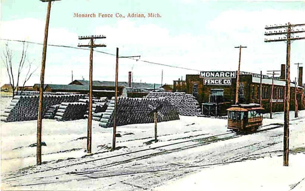 Eine von Schnee bedeckte Landschaft mit einem auf einer Spur fahrenden Fahrzeug, umgeben von Masten und einem Fabrikgebäude im Hintergrund mit Gegenständen auf dem Schnee hinter den Masten.