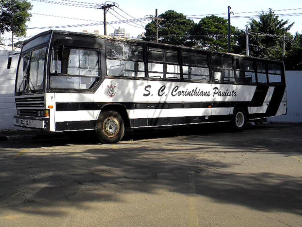 Ein Bus ist auf einer Straße mit einer Wand, Strommasten mit Kabeln, Bäumen, Gebäuden und dem Himmel im Hintergrund geparkt.