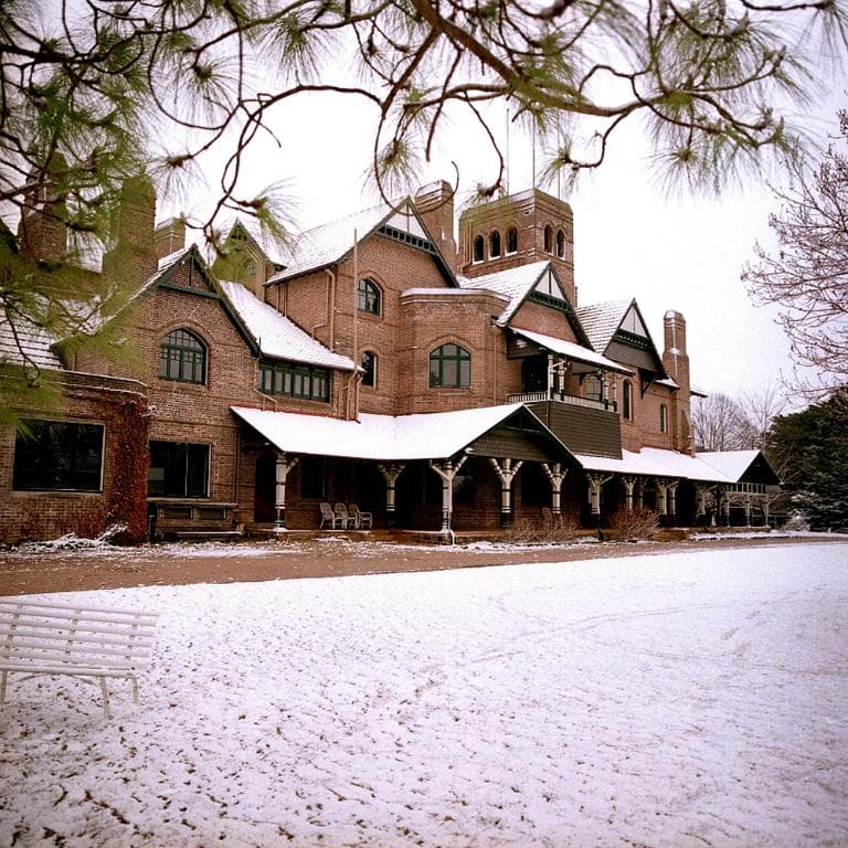 Ein Gebäude mit Fenstern und Säulen, Stühle davor, eine Bank und ein Zweigg auf der rechten Seite.