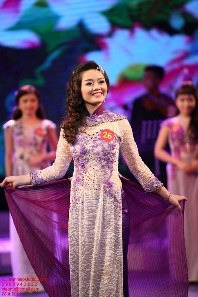 Eine Frau in einem cremefarbenen und lila Kleid mit einem Anstecker darauf, mit einem unscharfen Hintergrund.