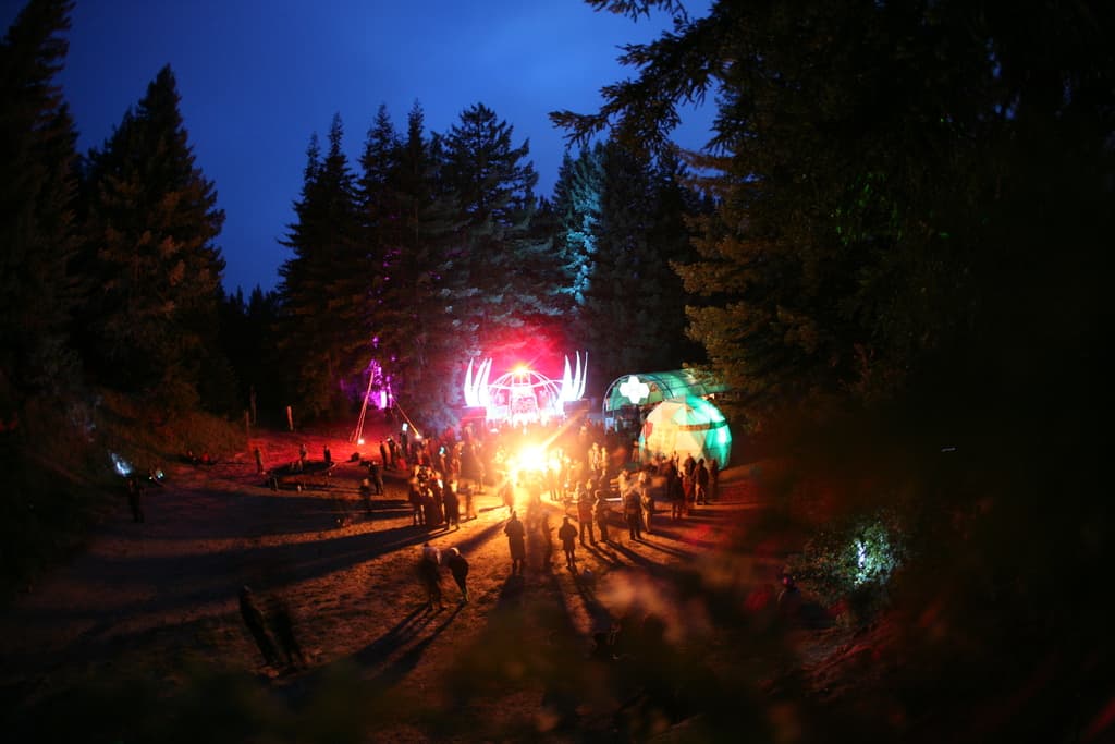 Eine Gruppe von Menschen, die eine Party mit roten und grünen Scheinwerfern in einer Hütte feiern, mit großen Bäumen im Hintergrund.