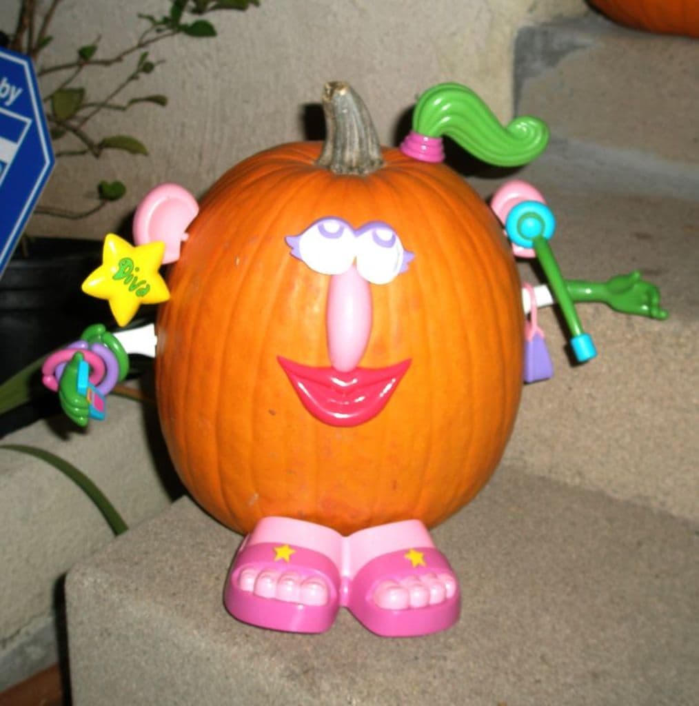 Eine Pumpkin sitzt auf einer Treppe mit Spielzeugen darauf, eine Pflanze und ein blaues Objekt links daneben und eine weitere Pumpkin darüber.