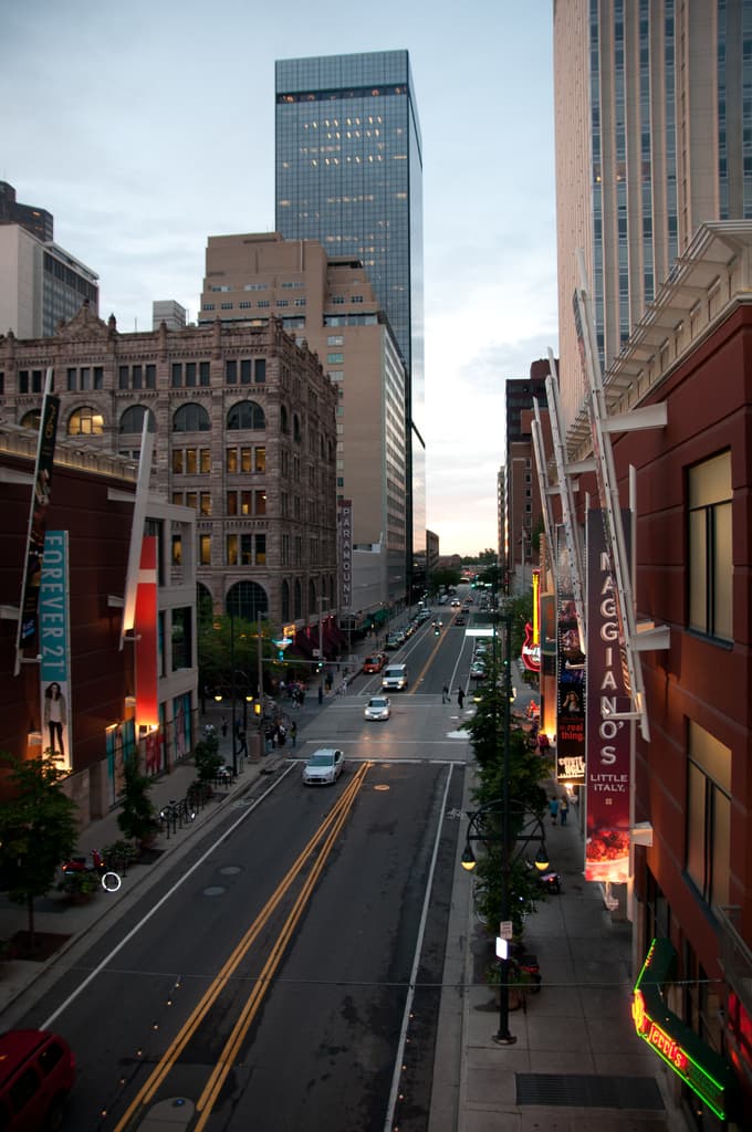 Eine Stadtansicht mit einer Straße voller Autos unten, flankiert von Gebäuden und Wolkenkratzern auf beiden Seiten, unter einem Himmel oben.
