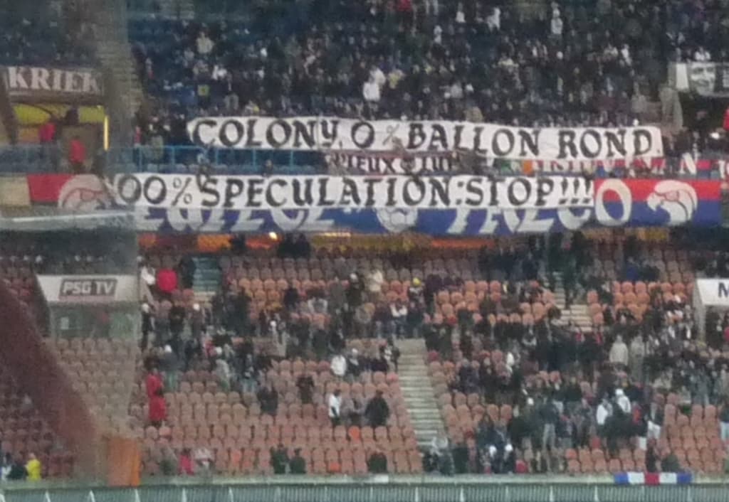 Ein Stadion voller großer Menge, Banner und Stühle, mit einem Zaun unten und Treppen auf der linken Seite.