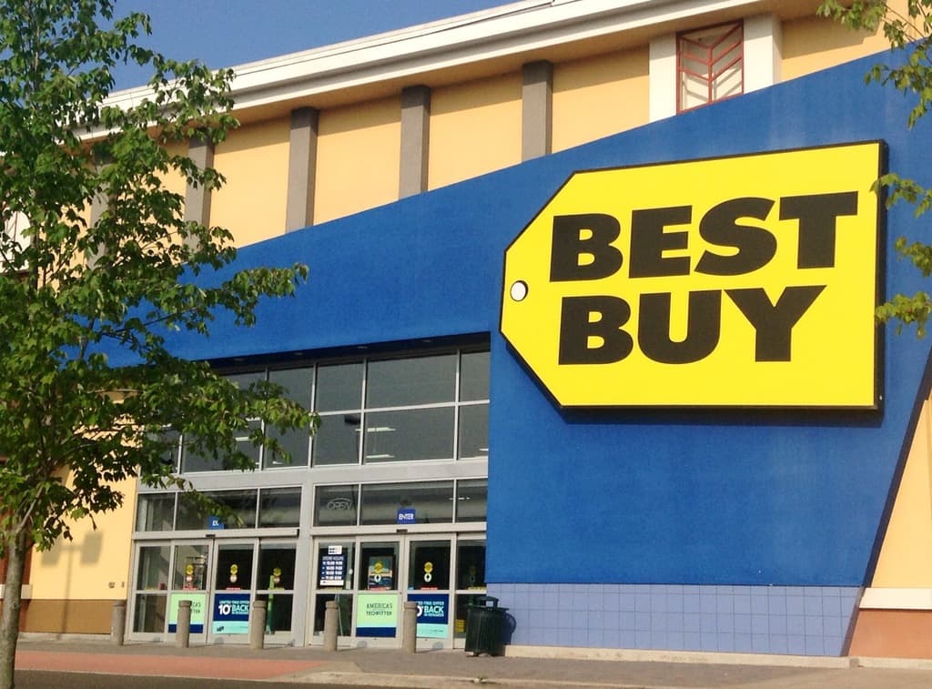 Ein Gebäude mit einem "Best Buy"-Schild, mehreren Bäumen davor und einer sichtbaren Tür.