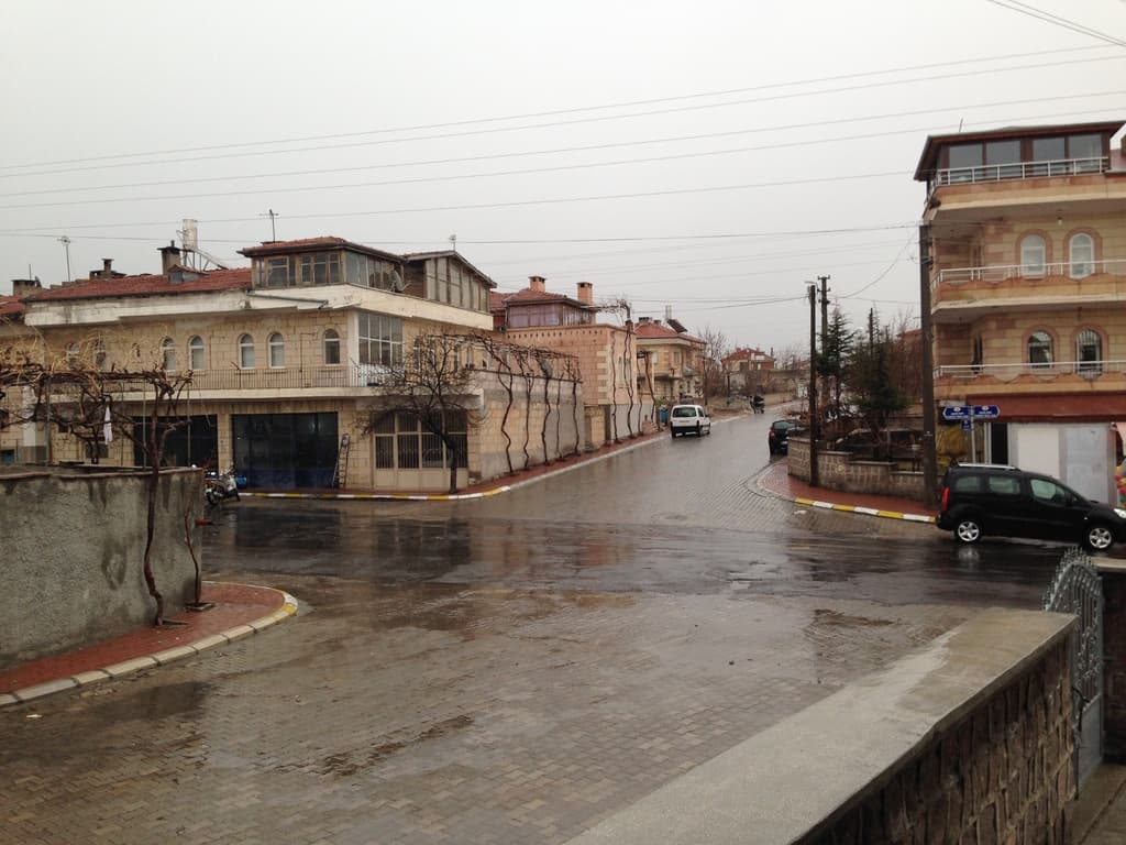 Eine Stadtansicht mit Kraftfahrzeugen auf Straßen, Gebäuden, Bäumen, Strommasten mit Kabeln, Geländern und Himmel.