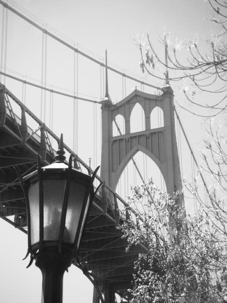 Ein altes Bild einer Hängebrücke mit einem schwarzen Laternenpfahl vorne unten und einem Baum in der rechten Ecke.
