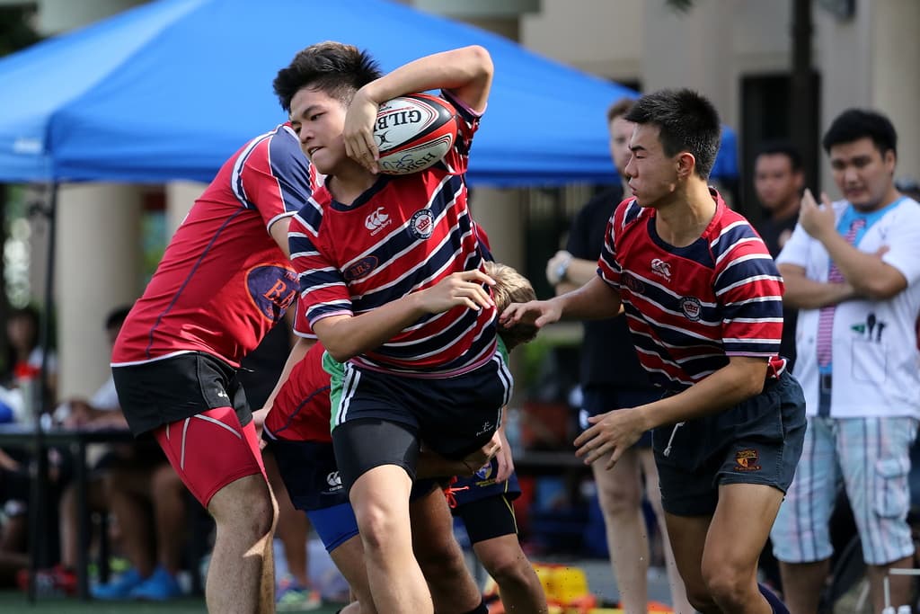 Eine Gruppe von Menschen, die draußen ein Spiel mit einem Jungen in der Mitte spielen, der einen Ball hält, während andere im Hintergrund stehen und zuschauen, neben einem blauen Zelt.