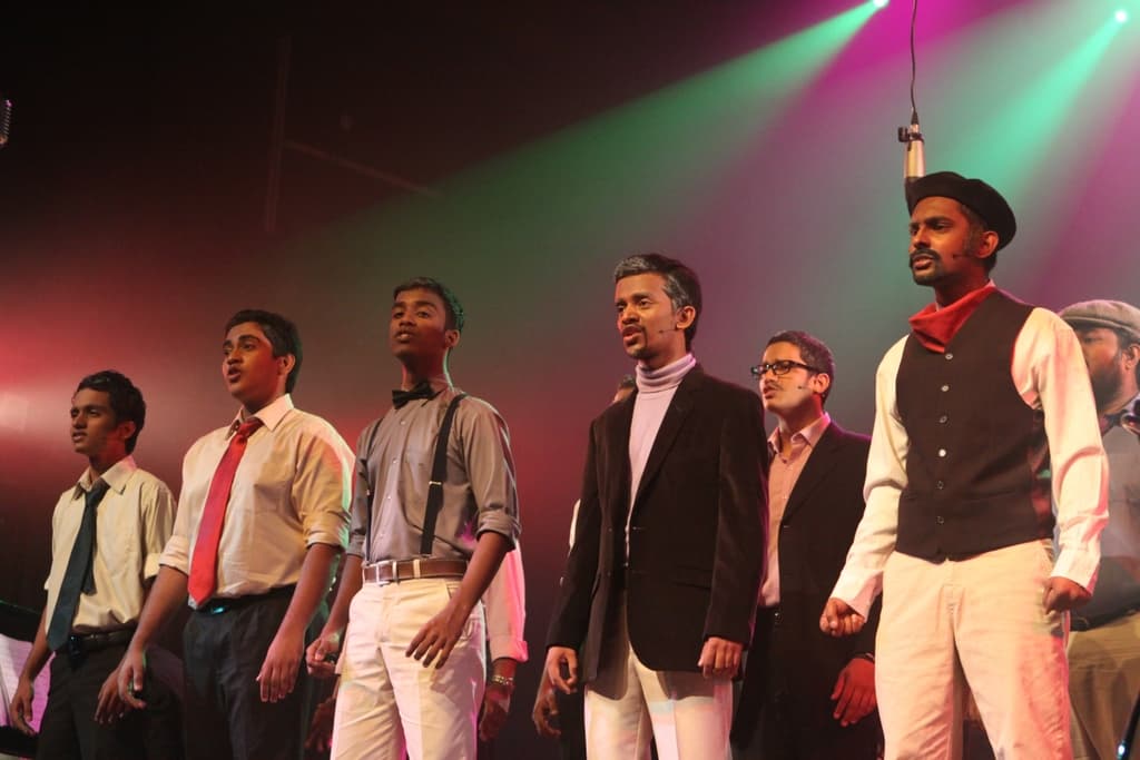 Eine Gruppe von Männern steht auf einer Bühne und spielt ein Drama mit grünen Scheinwerfern dahinter.