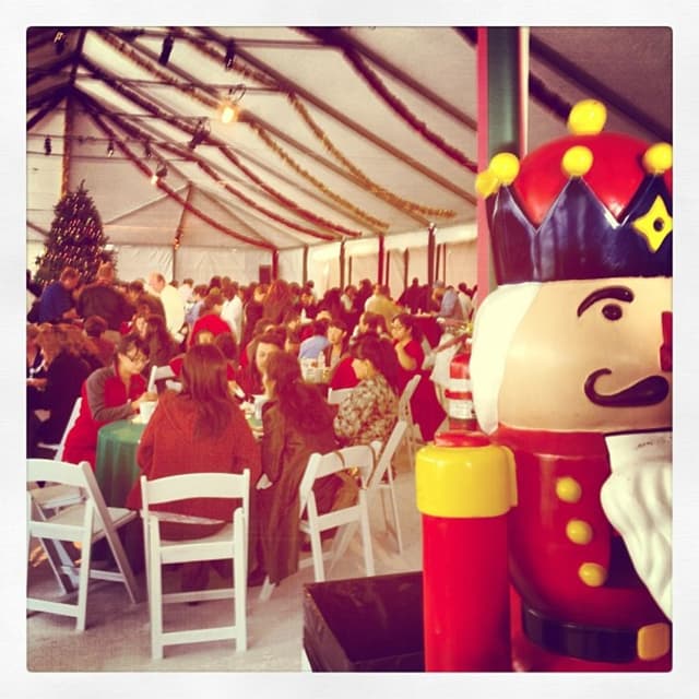 Eine Gruppe von Menschen feiert Weihnachten in einer Hütte, mit einem geschmückten Baum, weißen Stühlen, einem roten Spielzeug-Sicherheitsmann und einer schwarzen Krone.