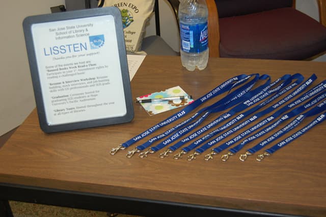 Ein Tisch mit ID-Kartenhaltern, ein Foto-Rahmen, eine Karte, ein Stift, eine Wasserflasche und ein Stuhl mit einer Tasche darauf.