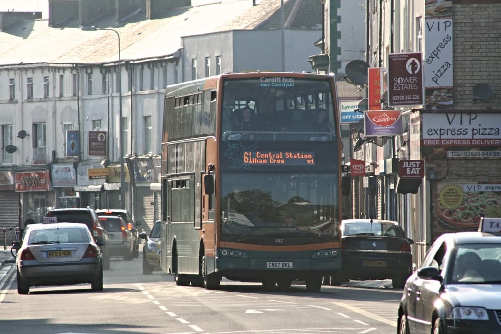 Eine Straße mit Autos und einem Bus vor Gebäuden mit Wänden, Fenstern, Tellern und Dächern, geschmückt mit Plakaten und Fahnen, mit einem Laternenmast im Blickfeld.