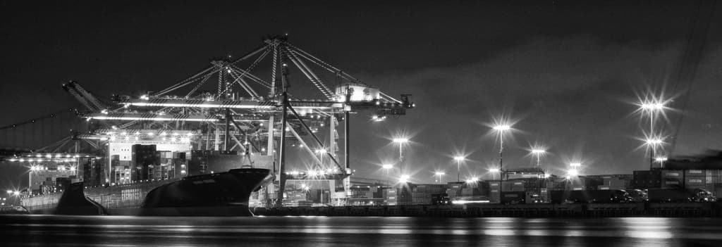 Ein Schiffbauwerk mit Metallstrukturen, Laternenmasten, Containern und Schiffen.