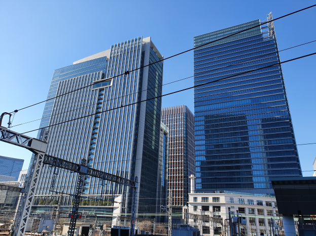 Eine Stadtstraße mit hohen Gebäuden, Strommasten, Drähten, Straßenlaternen, Ampeln, Namensschildern, Bäumen und einem klaren blauen Himmel.