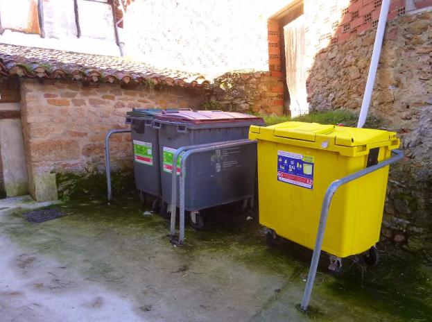 Zwei gelbe und graue Recyclingtonnen mit Rädern nebeneinander vor einem Gebäude mit einer Wand und einem Fenster.
