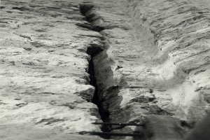 Schwarzes und weißes Foto eines großen Risses in einem Bodenkanal mit einem Wasserzeichen auf der linken Seite.