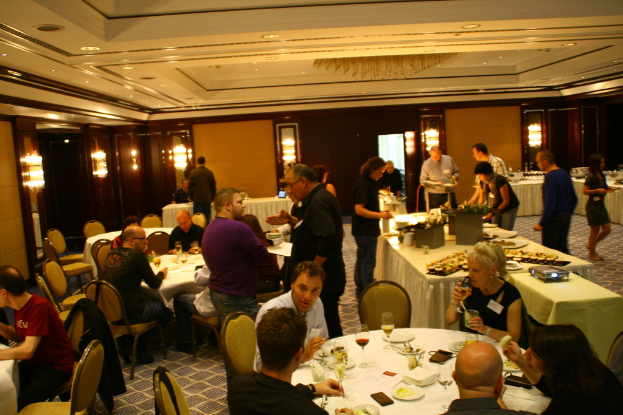 Ein Restaurant-Innenraum mit Tischen und Stühlen, Gruppen von Menschen beim Essen und einem zentralen Tisch mit verschiedenen Speisen, einige Menschen stehen und essen.