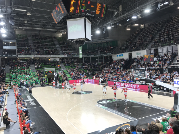 Basketballspiel in einer großen Arena mit Zuschauern, mit den Teams Asvel und Galatasaray, unter Stadionbeleuchtung und einem Scoreboard.