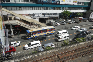Eine belebte Stadtstraße mit Fahrzeugen, Gebäuden, Grünflächen und diverser städtischer Infrastruktur.