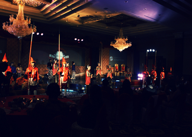 Eine Gruppe von Menschen, die eine Vorstellung mit zwei Kronleuchtern an der Decke anschauen.