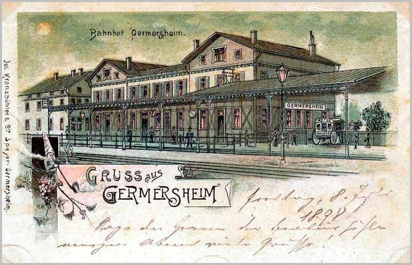 Schwarz-weiß-Postkarte vom Bahnhof Germersheim in Deutschland, die ein Bahnhofsgebäude, Menschen, Fahrzeuge, Bäume, einen Zaun, einen Straßenmast und einen bewölkten Himmel zeigt.