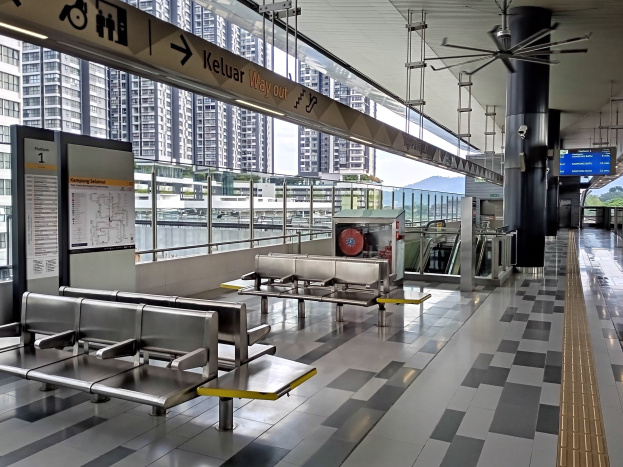 Leerer Flughafen Wartebereich mit mehreren Bänken, Informationsanzeigen, Säulen, Deckenventilator, Lampen und Hintergrundansicht von Gebäuden, Bäumen, Wasser und einem klaren blauen Himmel.