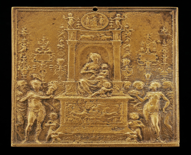 Goldene Plakette mit einer detaillierten Skulptur einer Frau in einem langen Kleid und einem Mann in Anzug und Krawatte auf schwarzem Hintergrund, umrahmt von einem prunkvollen goldenen Rahmen.