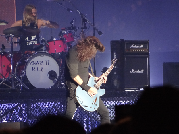 Charlie R.I.P. live auf der Bühne, Gitarre spielend und ins Mikrofon singend, mit einem Schlagzeuger im Hintergrund und Musikausrüstung einschließlich Lautsprechern und Instrumenten auf der Bühne.