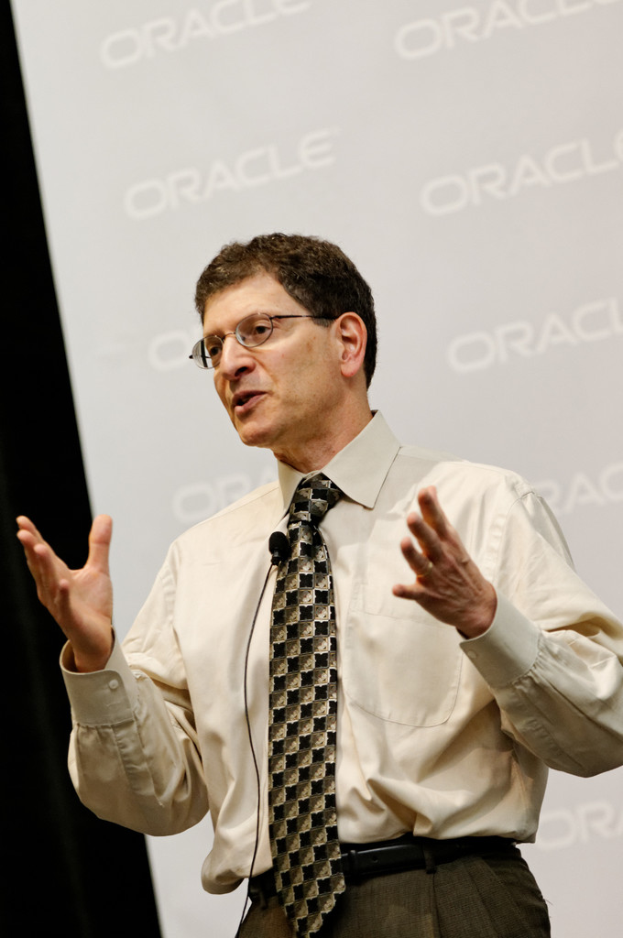 Eine Person steht vor einer Sponsor-Wand, trägt Kleidung und Brille.