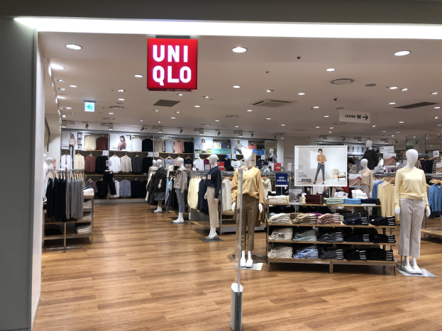 Innensicht eines Bekleidungsgeschäfts mit Schaufensterpuppen in Kleidung, Kleiderstücke an Bügeln, ein digitales Display, Informationsschilder, Deckenleuchten und ein "Uniqlo"-Ladenzeichen.