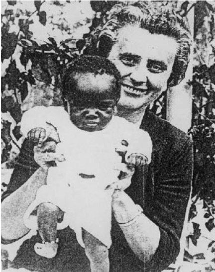 Ein Schwarz-Weiß-Foto einer Frau, die lacht, während sie ein Baby hält, mit Blättern im Hintergrund.