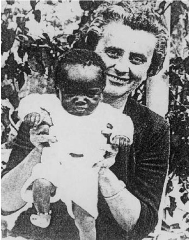 Ein Schwarz-Weiß-Foto einer Frau, die lacht, während sie ein Baby hält, mit Blättern im Hintergrund.