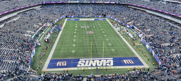 Ein volles Fußballstadion mit Zuschauern, Spielern auf dem Feld, Torpfosten und Werbetafeln unter hellen Stadionlichtern.