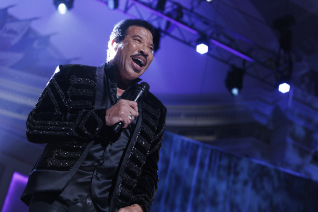 Lionel Richie performs bei den Grammys, trägt einen schwarzen Anzug und hält ein Mikrofon auf einer hell erleuchteten Bühne.