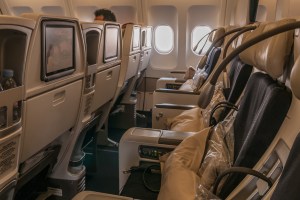 Eine Reihe leerer Business-Class-Flugzeugsitze mit einer Person an Bord, Fenster auf der rechten Seite zeigen eine Außenansicht.