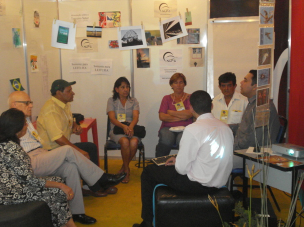 Eine Gruppe von Menschen, die auf Stühlen sitzen und diskutieren, mit Plakaten im Hintergrund.
