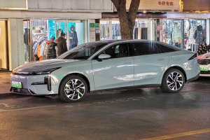 Ein Mitsubishi Lancer EV Elektroauto auf einer nächtlichen Straße geparkt, umgeben von Gebäuden, Geschäften, Schaufensterpuppen, Schildern und Lichtern.