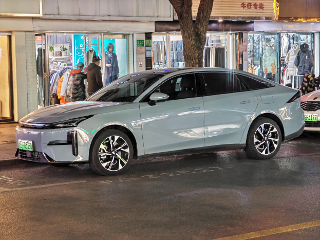 Ein Mitsubishi Lancer EV Elektroauto auf einer nächtlichen Straße geparkt, umgeben von Gebäuden, Geschäften, Schaufensterpuppen, Schildern und Lichtern.