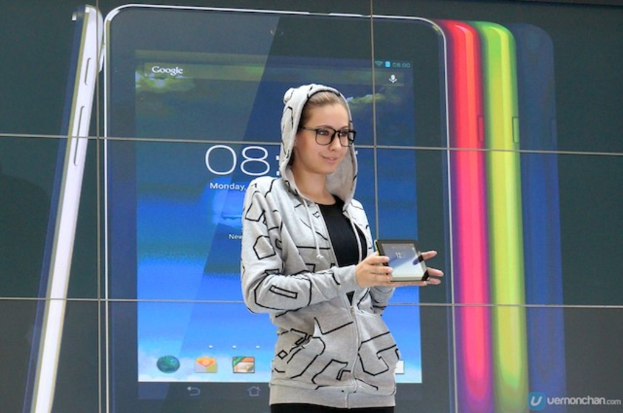 Eine Frau steht lachend und hält ein elektronisches Gerät mit sichtbarem Text auf dem Bildschirm.