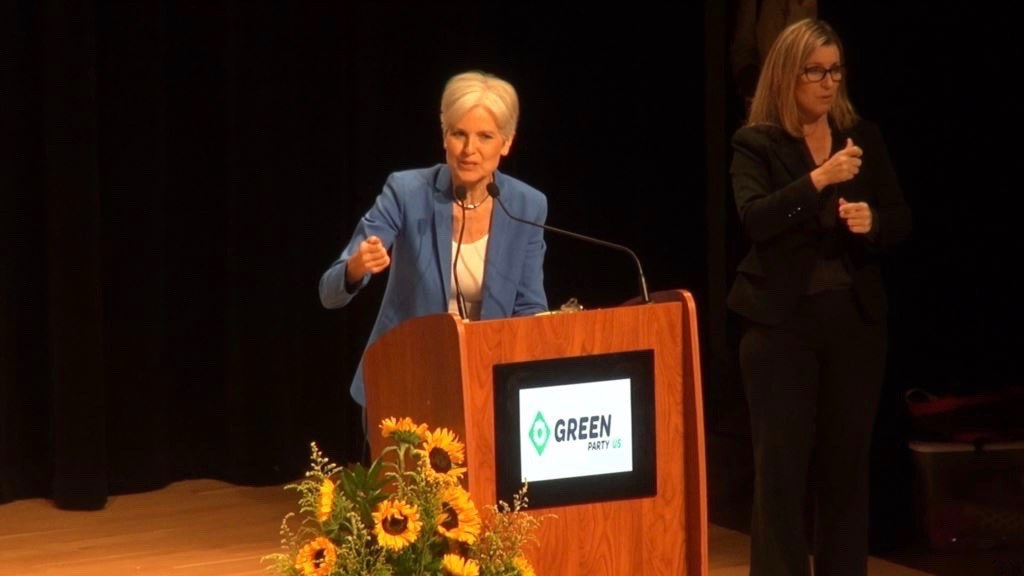 Zwei Frauen stehend an einem Podium mit Mikrofon, Bildschirm und Blumen bei einer Grünen-Veranstaltung, die die Umwelt nachhaltig gestalten diskutieren.