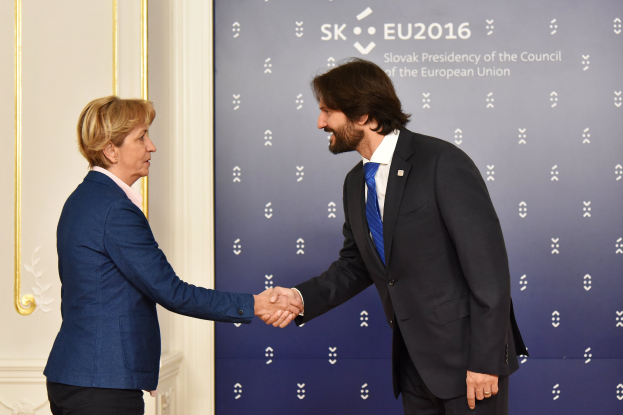 Bundeskanzlerin Angela Merkel und Bundespräsident Joachim Gauck geben sich die Hand vor einem 'EU-Gipfel'-Plakat.